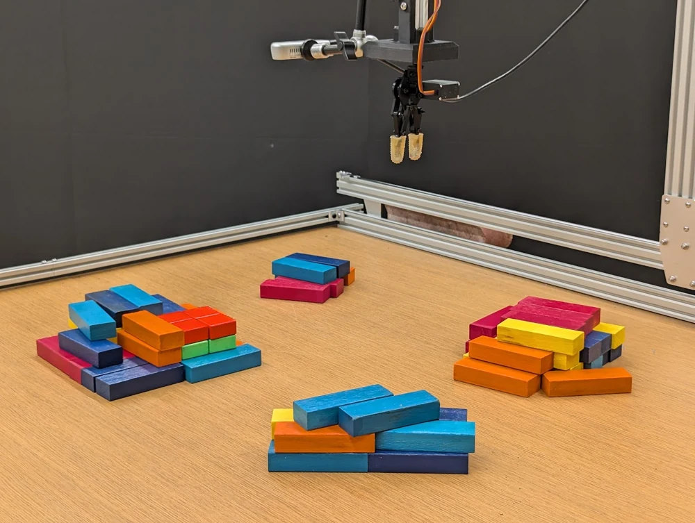 The gripper above four arrangements of colored blocks in the research workspace.