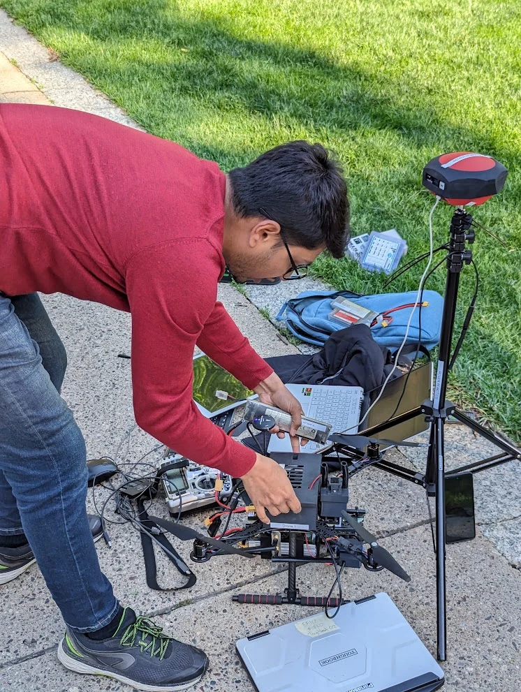 Preparing a drone outdoors with a laptop and positioning equipment.