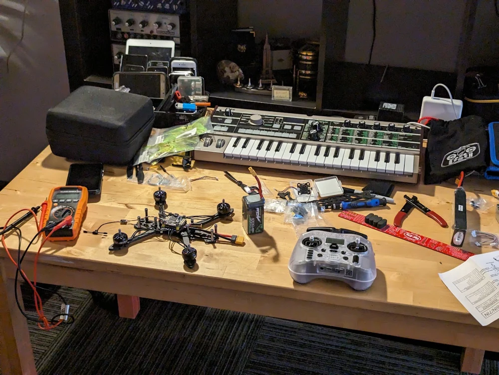 An FPV build in progress with the radio controller, battery, and test tools.