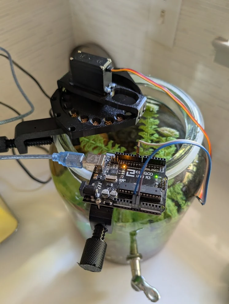 An early automated feeder and microcontroller mounted above a planted glass bowl.